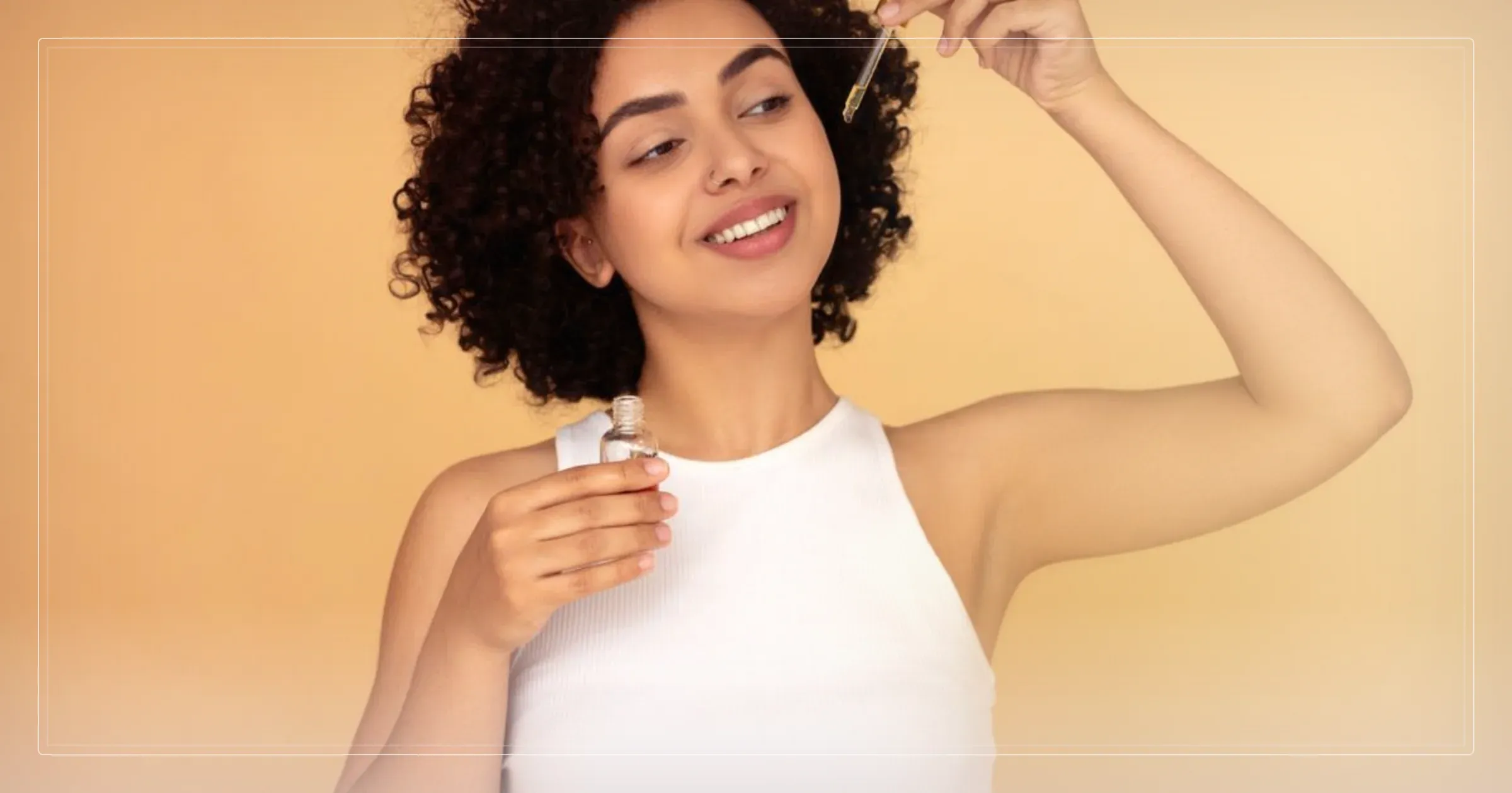 Femme souriante aux cheveux bouclés appliquant une huile de soin au compte-gouttes, ambiance douce et dorée